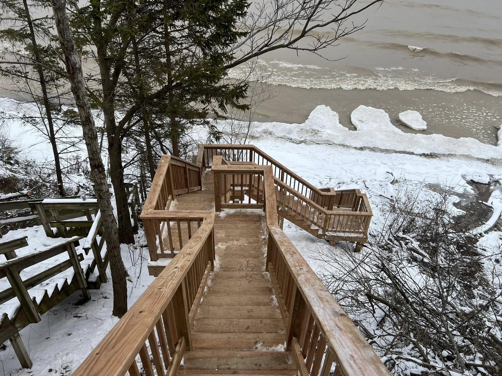 Newly built wooden staircase leading to a snowy Lake Michigan shoreline in Sheboygan, WI by IW Brothers LLC.